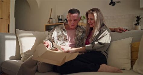 A Happy Middle Aged Man And His Mature Wife Are Sitting On The Sofa And Looking At Old