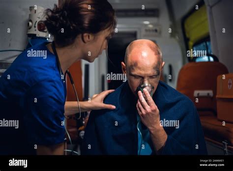 Nurse In Blue Medical Uniform Puts Her Hand On Man Who Sits In Oxygen