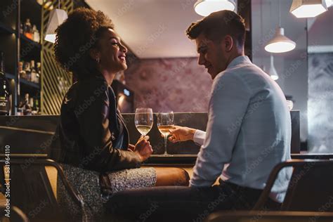 Romantic Couple On A Date Talking Holding A Glass Of White Wine Sitting At The Bar Counter In