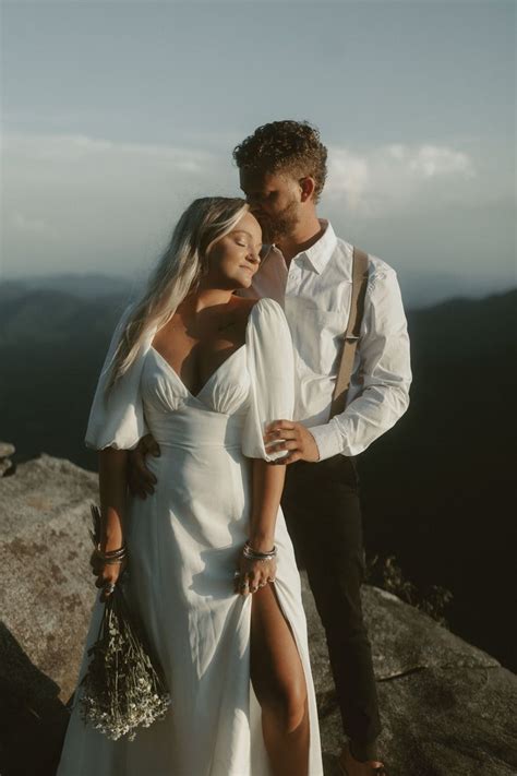 A Man And Woman Standing On Top Of A Mountain Next To Each Other With