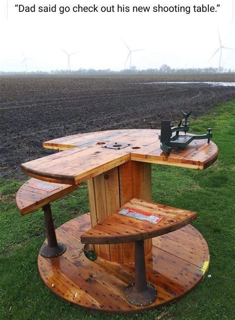 A Wooden Table Sitting In The Middle Of A Field With Wind Turbines