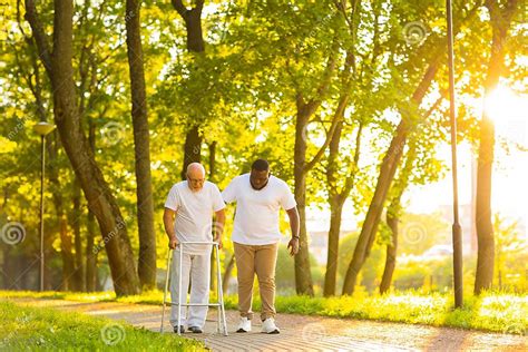 Caregiver Is Teaching Old Man To Walk With Walker Professional Nurse