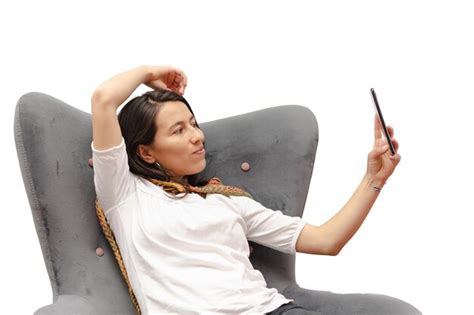 Mujer latina sentada en una silla bonita tomando una foto con su teléfono celular aislado de