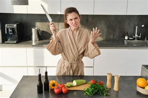 Boze brunette vrouw met mes in de keuken geïrriteerd en gefrustreerd om te koken boos makend