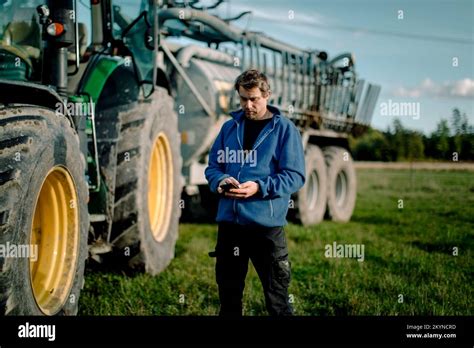 Mature Farmer Using Smart Phone Standing Against Tractor On Field Stock