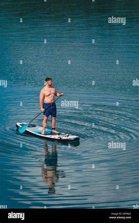 Man Balancing On Supboard Paddling On The Middle Of The Lake Water