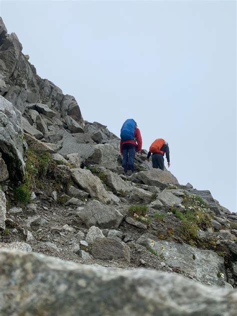 Two People Climbing Up The Side Of A Rocky Mountain