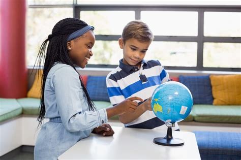 Niños de la escuela mirando el globo en la biblioteca Foto Premium