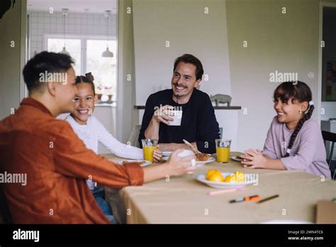 Happy Gay Couple Spending Leisure Time With Daughters While Having Breakfast At Dining Table In