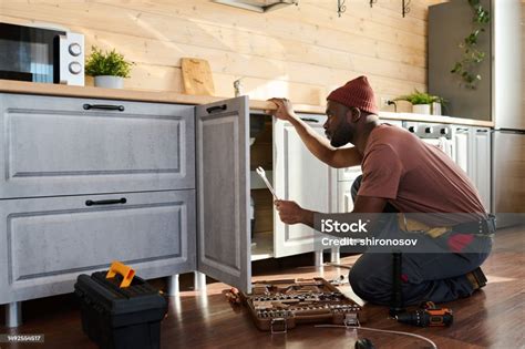 Side View Of Young African American Repairman Checking Pipes Stock