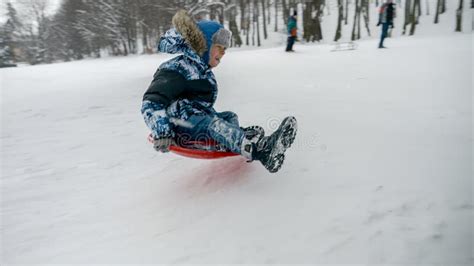 Young Boy Laughing And Smiling While Sledding Down A Snowy Hill And