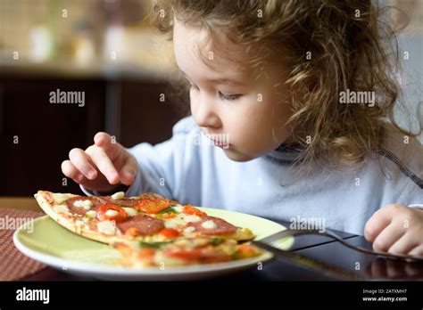 El niño mira la pizza en la mesa Niño de tres años va a comer por sí