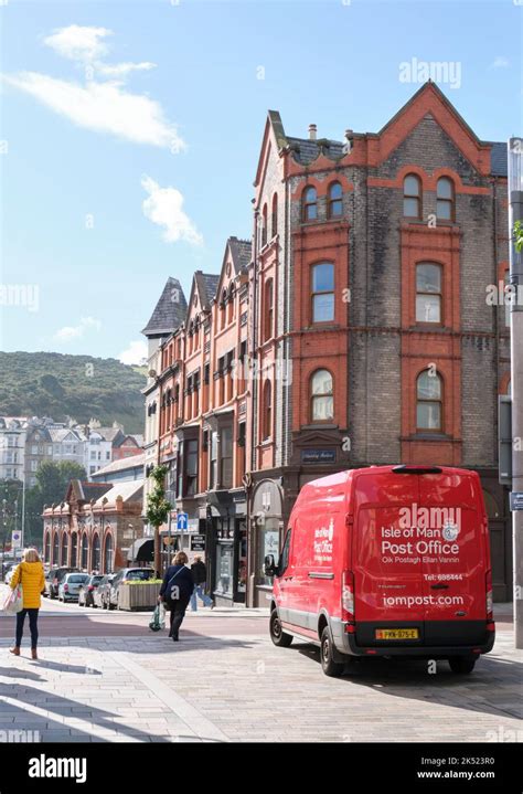 A distinctive red post office van in Douglas town centre, isle of man with victorian buildings ...