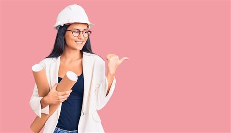 Joven Hermosa Chica Latina Con Casco De Arquitecto Sosteniendo Planos Apuntando Con El Pulgar