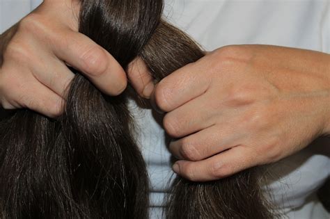 Una chica con cabello largo y oscuro está trenzando su cabello manos de