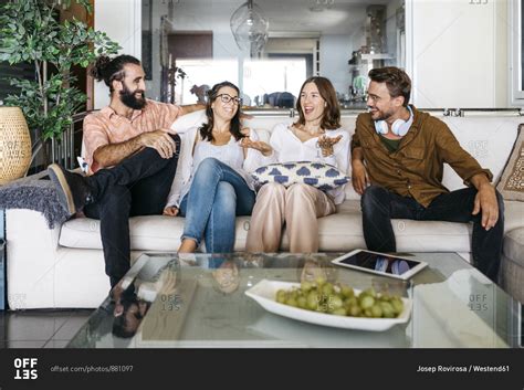 Happy friends sitting on couch together and talking stock photo - OFFSET