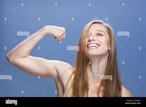 Skinny Brunette Girl Showing Muscles And Smiling Studio Portrait Against Blue Background Stock