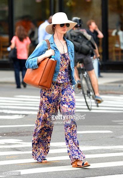 A Woman Crossing The Street Wearing A Hat And Carrying A Brown Bag In