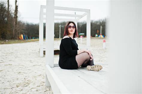 Portrait Of Brunette Girl In Black Dress Sitting At White Wooden Construction Stock