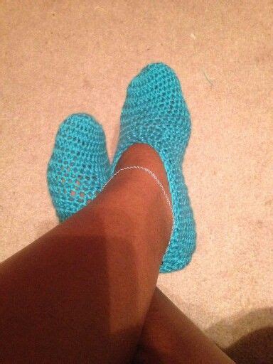 A Person S Feet Wearing Blue Crochet Slippers On The Floor Next To A