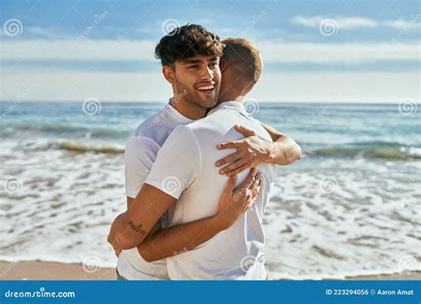 Jovem Casal Gay Sorrindo Feliz Abra Ando Na Praia Foto De Stock