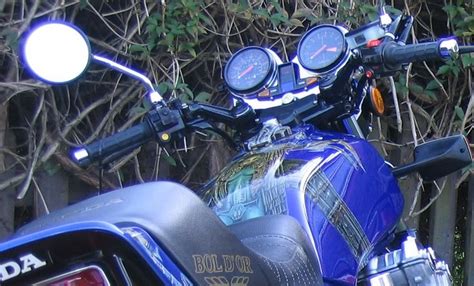 A Blue Motorcycle Parked In Front Of A Wooden Fence And Shrubbery With