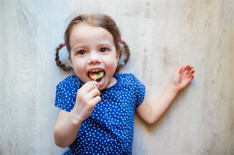 Menina Que Encontra Se No Assoalho Sorrindo Comendo O Pirulito Imagem