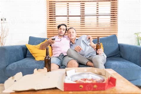 deux gay Hommes dans décontractée tenues séance sur canapé embrassement et en train de regarder