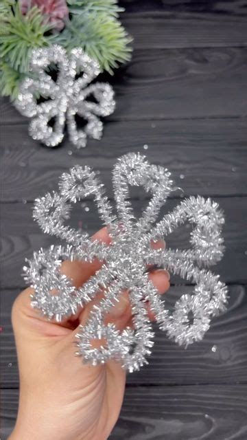 A Hand Holding A Snowflake On Top Of A Wooden Table Next To Flowers