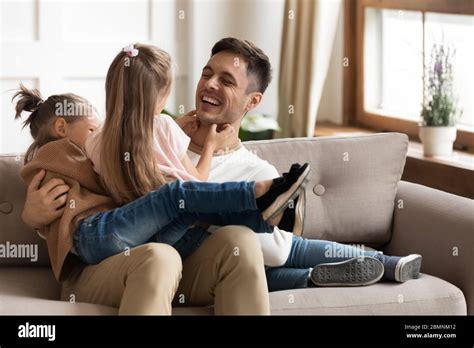 Happy Father Playing With Two Daughters Tickling On Couch Stock Photo