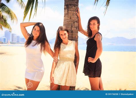 Trois Filles Minces De Brune Se Tiennent Nu Pieds Sur La Plage Photo