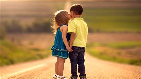 Little Girl Is Kissing Boy Wearing Blue Yellow Dress In Green Blur