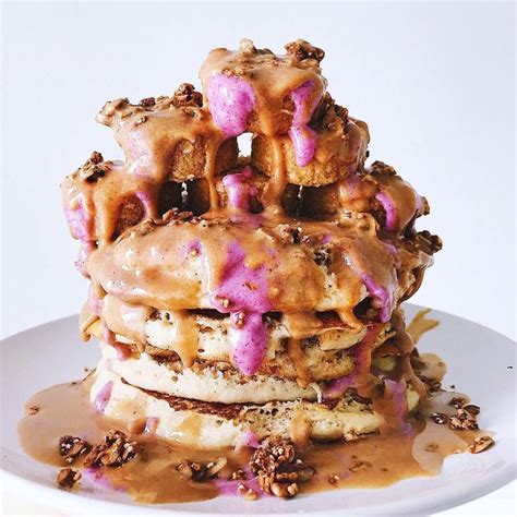 A Stack Of Waffles Covered In Pink Frosting And Nuts On A White Plate