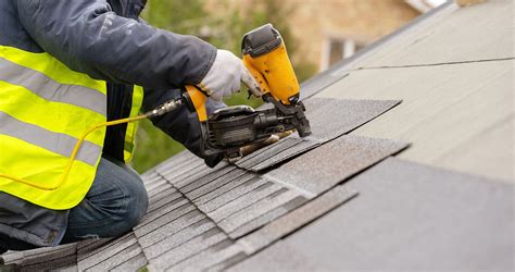 Workman using pneumatic nail gun install tile on roof of new hou ...