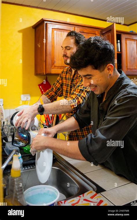 A Loving Gay Couple Shares A Light Moment While Doing Dishes Together In A Bright Kitchen