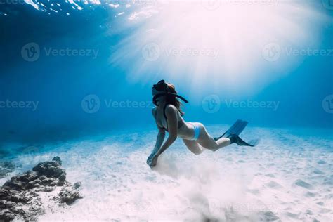 Freediver Woman With Fins Glides Over Sandy Sea Bottom In Sea