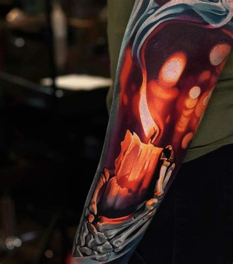 A Man With A Tattoo On His Arm Holding A Lit Candle In Front Of Him