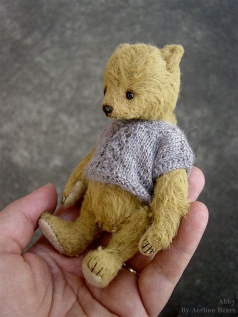 A Small Teddy Bear Wearing A Sweater In Someone S Hand