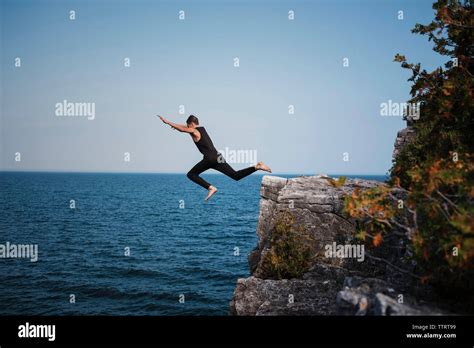 Full length of hiker cliff jumping against sea and clear sky at Bruce ...