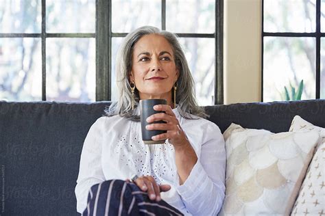 Mature Woman With Grey Hair Relaxing And Drinking Tea In Her Living Room By Stocksy