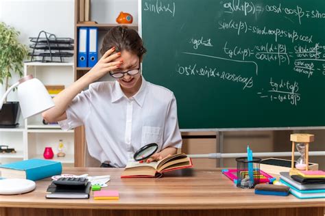 Jeune enseignante de mathématiques blonde stressée portant des lunettes assise au bureau avec