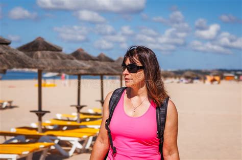 Fit And Vital Mature Woman Is Choosing Deck Chair With Parasol For Relaxing On The Beach Stock
