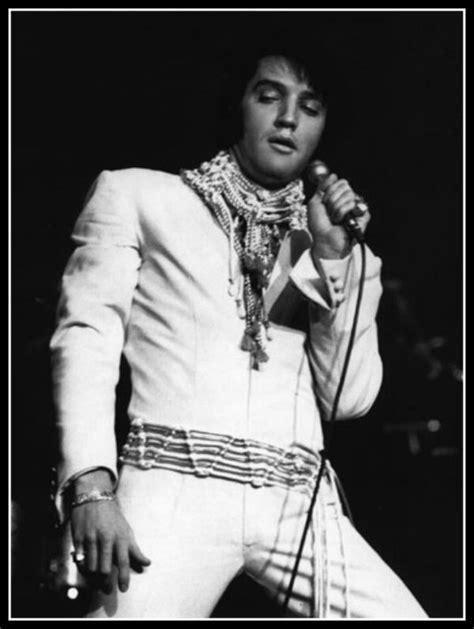 Elvis Presley Singing Into A Microphone In His White Suit And Scarf On Stage At A Concert