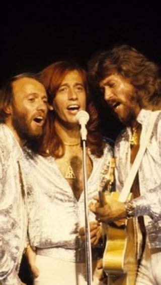 The Bee Gees Singing Into A Microphone While Standing Next To Each