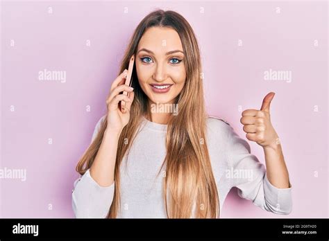 Junge blonde Mädchen mit Gespräch auf dem Smartphone lächeln glücklich und positiv Daumen nach