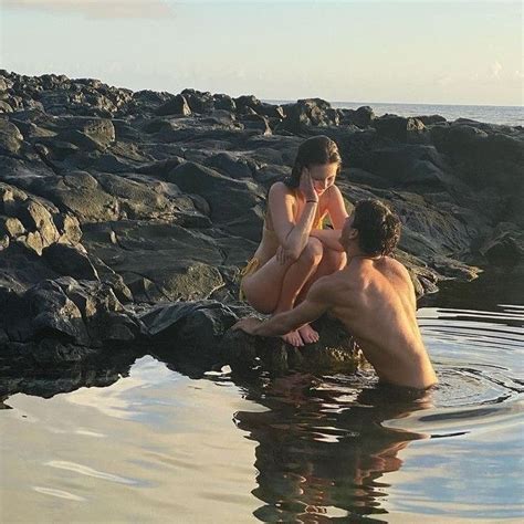 Two People Are Sitting In The Water Near Some Rocks And One Is Talking