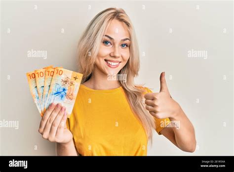 Schöne kaukasische blonde Mädchen hält schweizer Franken Banknoten lächeln glücklich und