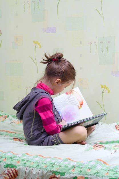 Menina criança sentada na cama lendo um livro Foto Premium