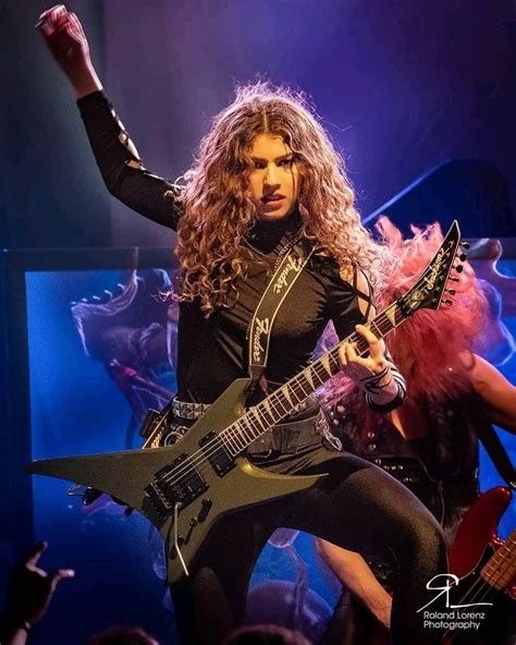 a woman with long hair holding a guitar in front of her and performing ...