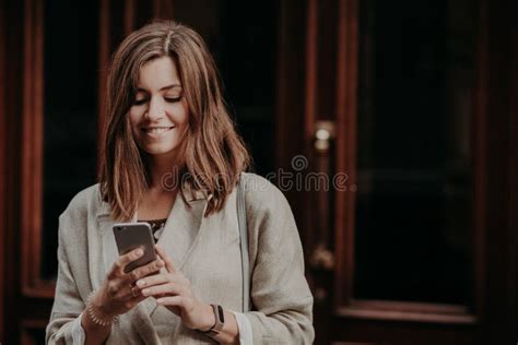 Horizontal Shot Of Pretty Cute Brunette Female Model Shares Multimedia Files Via Cell Phone